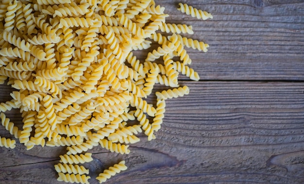 Pasta raw macaroni on wooden background close up raw macaroni spiral pasta uncooked delicious fusilli pasta for cooking food top view