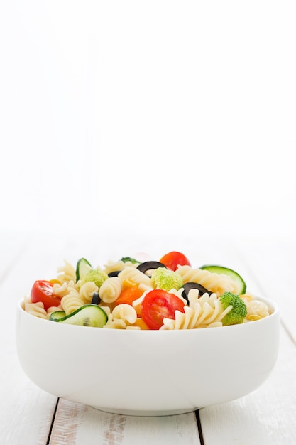 Photo pasta salad in a bowl on white wooden table copy space