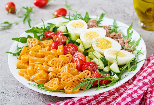 Pasta salad with fresh vegetables, eggs and tuna in a white bowl. Lunch food.