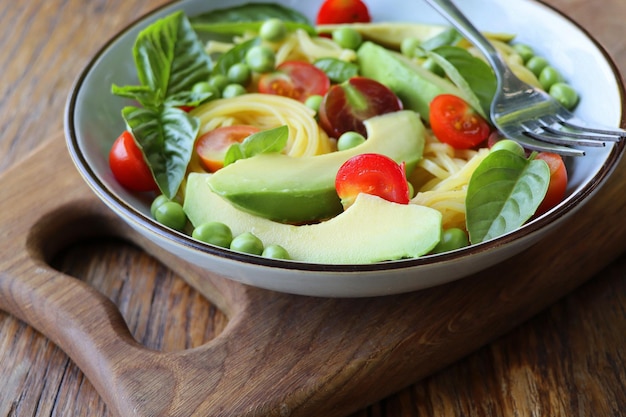 Photo pasta salad with green peas avocado cherry tomatoes and basil on rustic wooden background top view