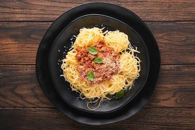 Pasta spaghetti Bolognese Tasty appetizing italian spaghetti with bolognese sauce tomato sauce cheese parmesan and basil on white plate on old wooden rustic table background Top view