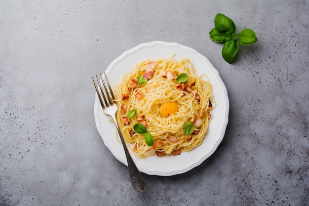 Pasta spaghetti carbonara with bacon, parmesan cheese, egg yolk and basil leaves on gray light surface. Traditional Italian dish