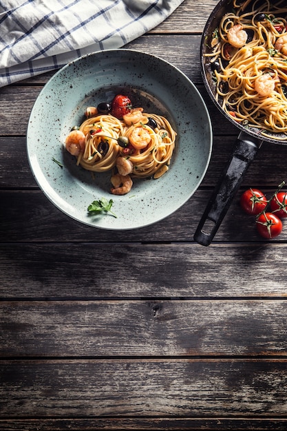 Pasta spaghetti on plate and pan with shrimp tomato sauce toatoes and herbs. Italian or mediterranean cuisine.