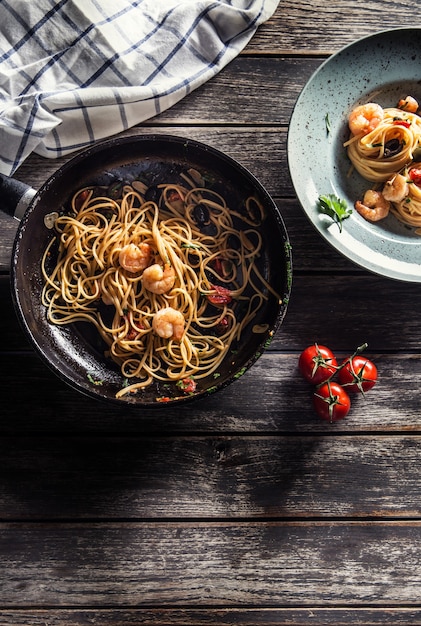 Pasta spaghetti on plate and pan with shrimp tomato sauce toatoes and herbs. Italian or mediterranean cuisine.