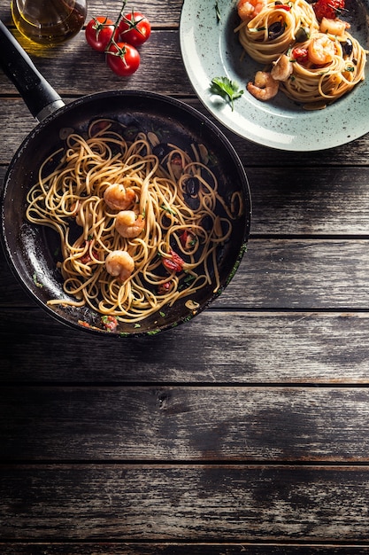 Pasta spaghetti on plate and pan with shrimp tomato sauce toatoes and herbs. Italian or mediterranean cuisine.