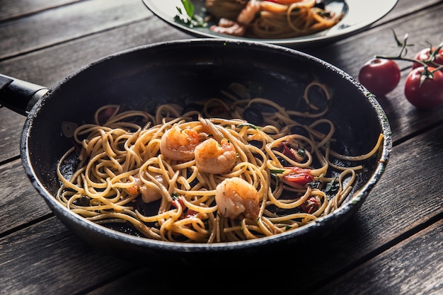 Pasta spaghetti on plate and pan with shrimp tomato sauce toatoes and herbs. Italian or mediterranean cuisine.