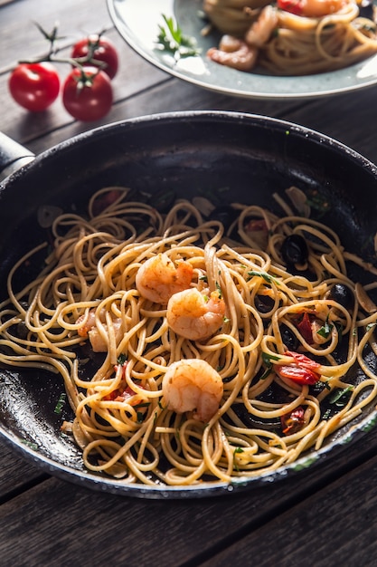 Pasta spaghetti on plate and pan with shrimp tomato sauce toatoes and herbs. Italian or mediterranean cuisine.