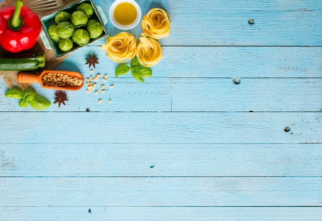 Pasta tagliatelle with pesto sauce and other vegetables on a wood background. Top view