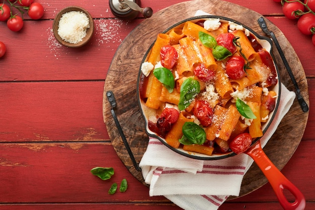 Pasta Tortiglioni with tomato sauce baked cherry tomatoes mozzarella and parmesan cheese basil on old red rustic table Traditional Italian cuisine Example Italian food for article Top view