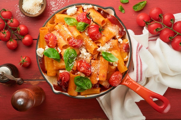 Pasta Tortiglioni with tomato sauce baked cherry tomatoes mozzarella and parmesan cheese basil on old red rustic table Traditional Italian cuisine Example Italian food for article Top view