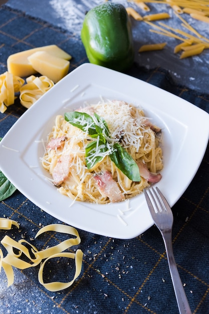 Pasta with bacon, cream, basil, parmesan, garlic, egg (yolk) on white plate