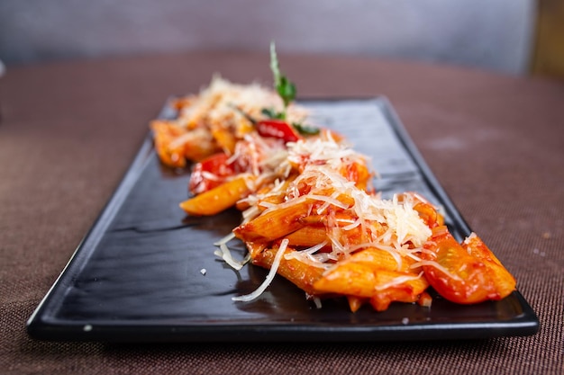 Pasta with cheese and stewed tomatoes on a black plate