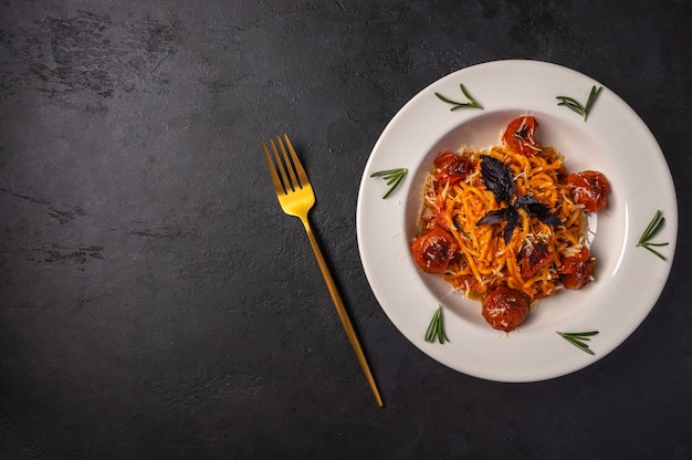 Pasta with cherry tomatoes, cheese and rosemary served on plate with fork on dark textured