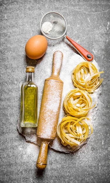 Pasta with olive oil, sieve, rolling pin and flour on a stone stand. On the stone table. Top view