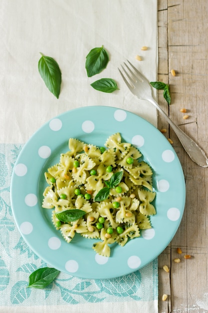 Pasta with pesto sauce, green peas and basil on a wooden table