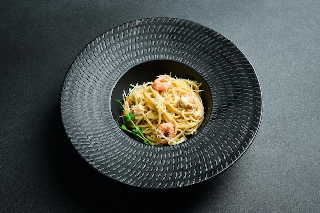 Photo pasta with shrimp and cheese in a black bowl on a dark background closeup