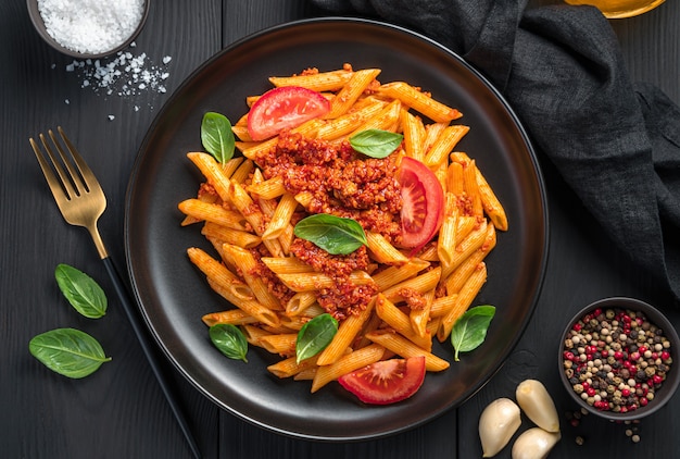 Pasta with tomato bolognese sauce and fresh basil on a black background. A traditional Italian dish.