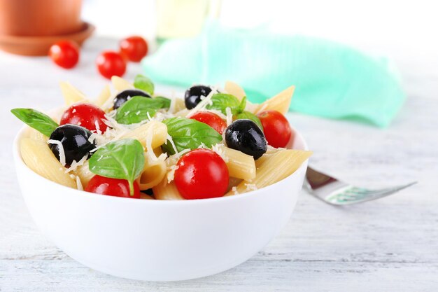 Pasta with tomatoes olives and basil leaves in bowl on napkin on wooden table on natural background