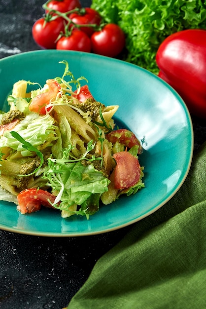 Pasta with vegetables tomatoes and pesto in a plate on a dark background Salad with pasta