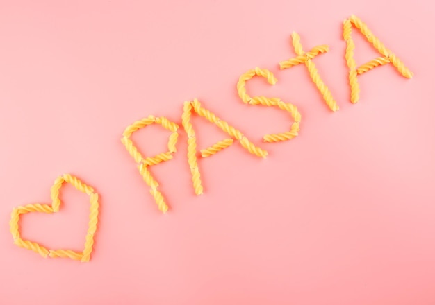 Photo pasta word made with fusilli on pink background