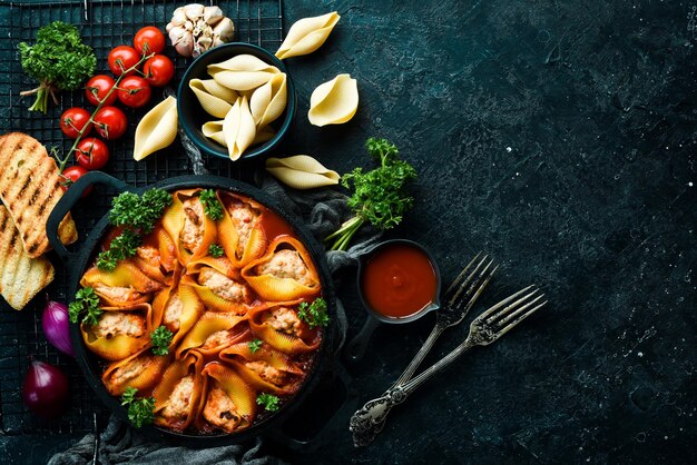 Paste Large pasta shells baked with meat in tomato sauce In a frying pan On a black stone background