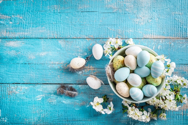 Pastel colored Easter eggs and spring blooming branches on blue wooden.