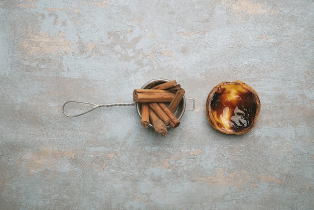 Pastel de nata. Traditional Portuguese dessert, egg tart over rustic background with cinnamon sticks in the strainer. Top view