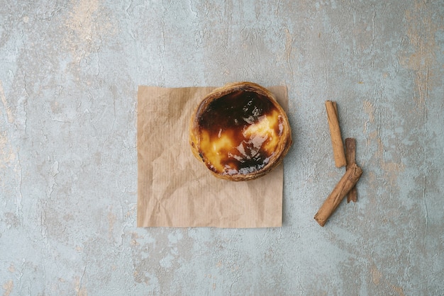 Pastel de nata. Traditional Portuguese dessert, egg tart on the sheet of baking paper over rustic background with cinnamon sticks. Top view