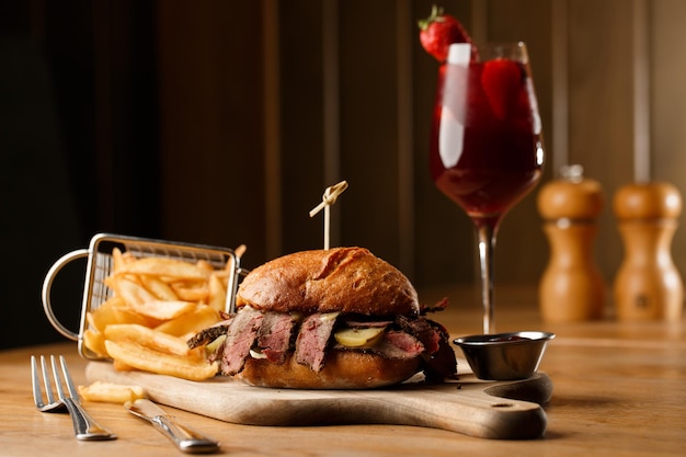 Pastrami sandwich on rye bread served with pickles and mustard sauce Tasty sandwich with french fries potatoes and Sangria drink on dark background