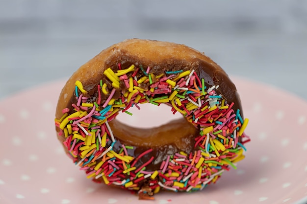 Pastries concept. Donuts with chocolate glaze with colorfull sprinkles, on a pink plate. side view