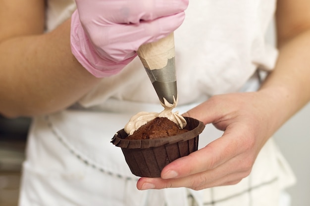 Pastry chef applies cream to chocolate muffin