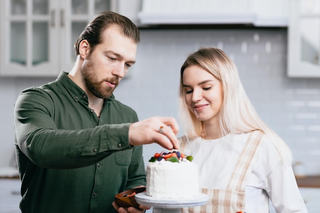 Pastry chef confectioner young caucasian woman with husband boyfriend man try taste of cake on kitchen table Cakes cupcakes and sweet dessert