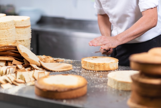 Pastry chef cutting the sponge cake on layers. Cake production process.