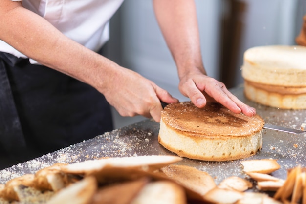 Pastry chef cutting the sponge cake on layers. Cake production process.