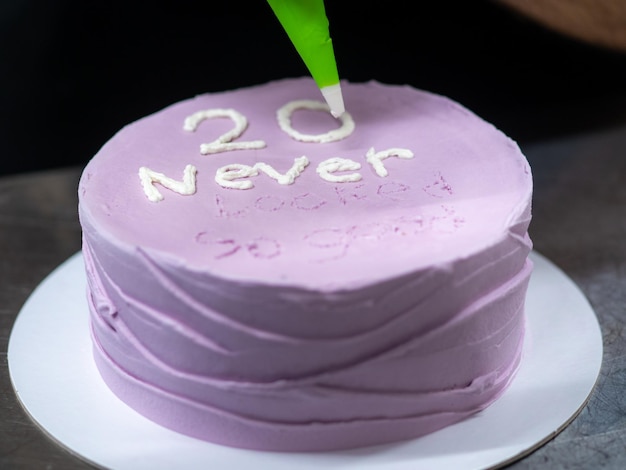 Pastry chef decorating a purple frosted birthday cake with text topping