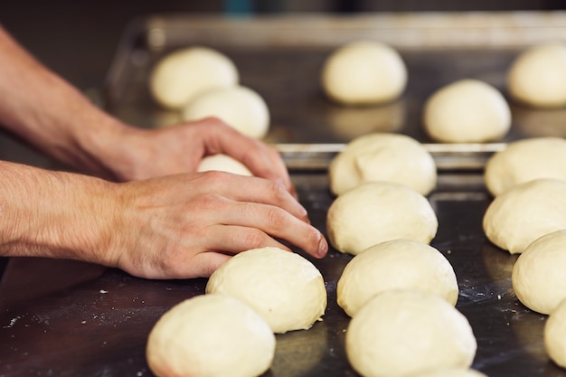 Pastry chef forms round buns from dough and spreads them on metal pan.