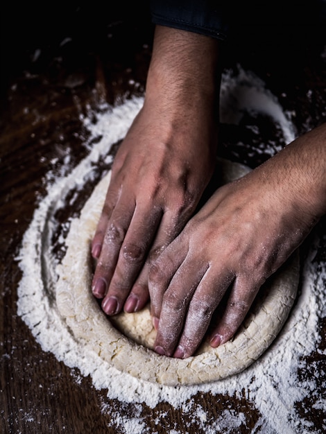 Pastry chef hand kneading Raw Dough with sprinkling white flour over kitchen table.