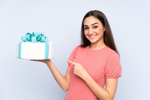 Pastry chef holding a big cake isolated on blue background and pointing it