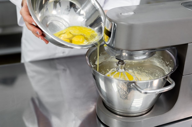 Pastry chef poured the eggs in the kitchen machine mixer