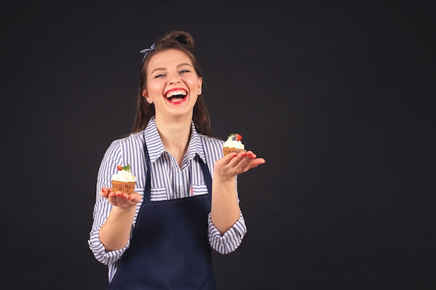 Pastry chef smiles at the camera in the Studio on a black background holding cupcakes in bunches