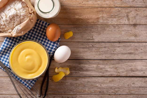 Pastry cream in a bowl and ingredients on wooden table