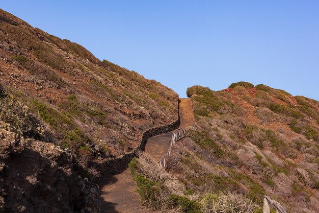 Path to the Volcano Monte Nero of Linosa. Characteristic country road with the dry stone wall built with lava stones