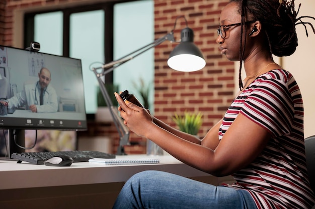 Patient discussing prescripted medicaments with doctor on video call, woman talking with therapist online, holding pills bottle. Telemedicine, remote general practitioner appointment