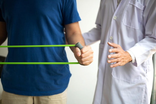 Patient doing stretching exercise with a flexible exercise band and a physical therapist hand to help in clinic room