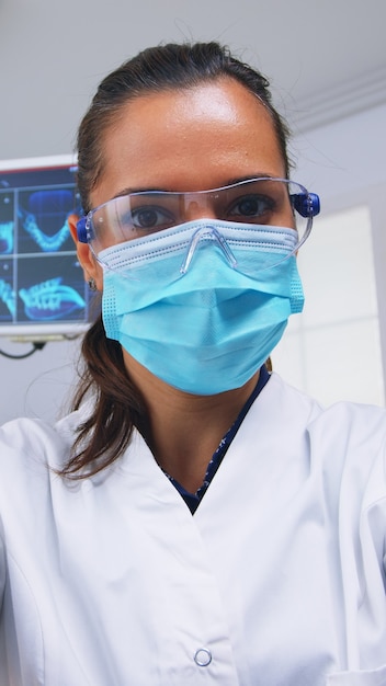 Patient pov to stomatologist performing examination and taking care of teeth using dental tools in modern clinic. Doctor and nurse working in modern orthodontic office wearing protection mask