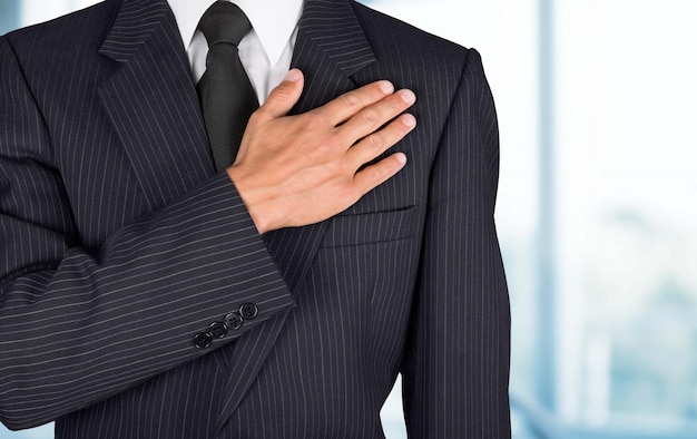 Patriot man against office background, holding palm on heart