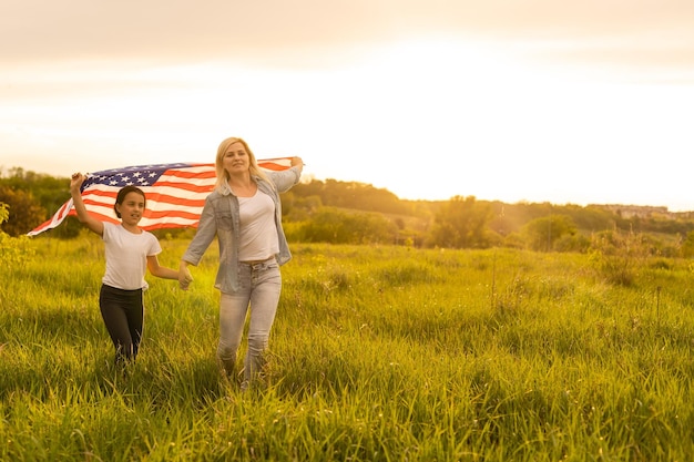 Patriotic holiday. Happy family, mother and her daughter child girl with American flag outdoors. USA celebrate 4th of July.