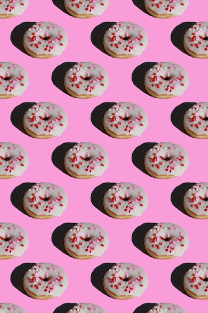 pattern of glazed donuts covered with heart sprinkles on pink background