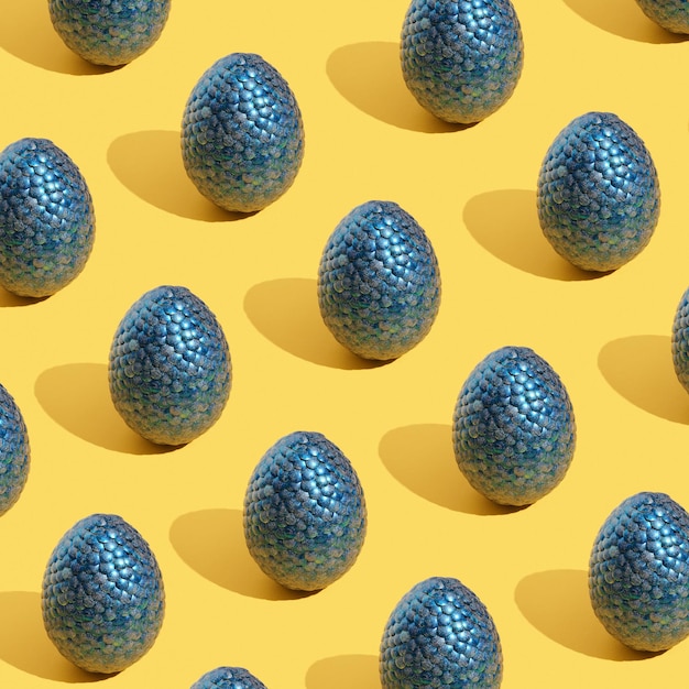 Pattern made with blue shiny eggs on yellow background Positive mood happiness and festive inspiration