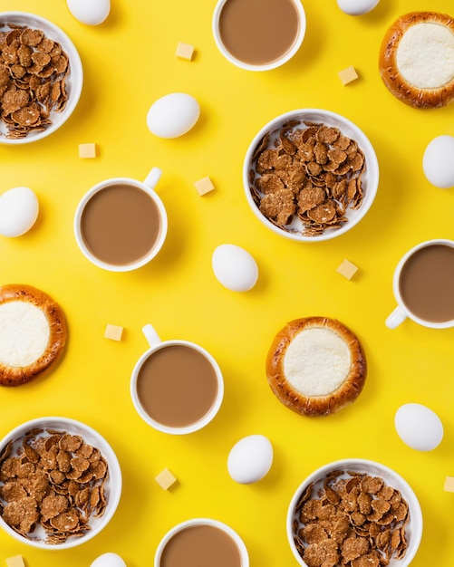 Pattern made with bowls of oatmeal coffee cups buns with cottage cheese eggs and cheese cubes on yellow background Creative breakfast concept top view